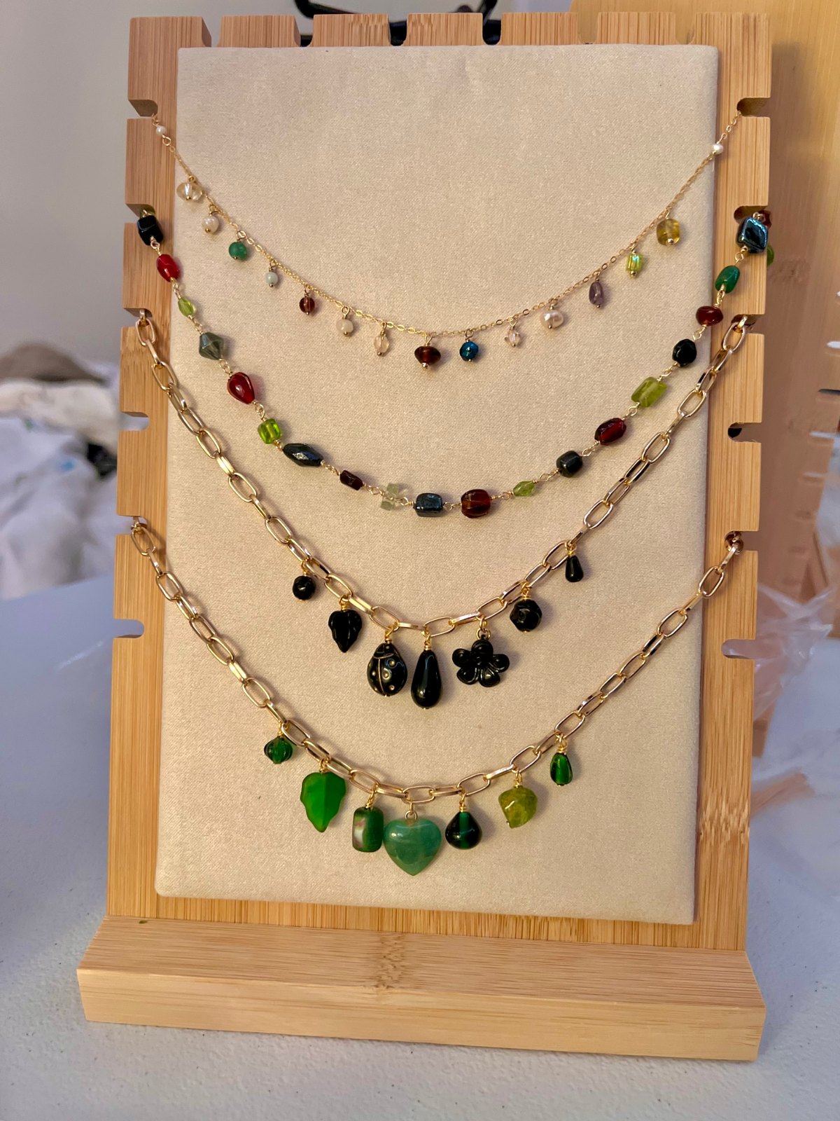 Four layered beaded necklaces in jewel tones displayed on a bamboo stand