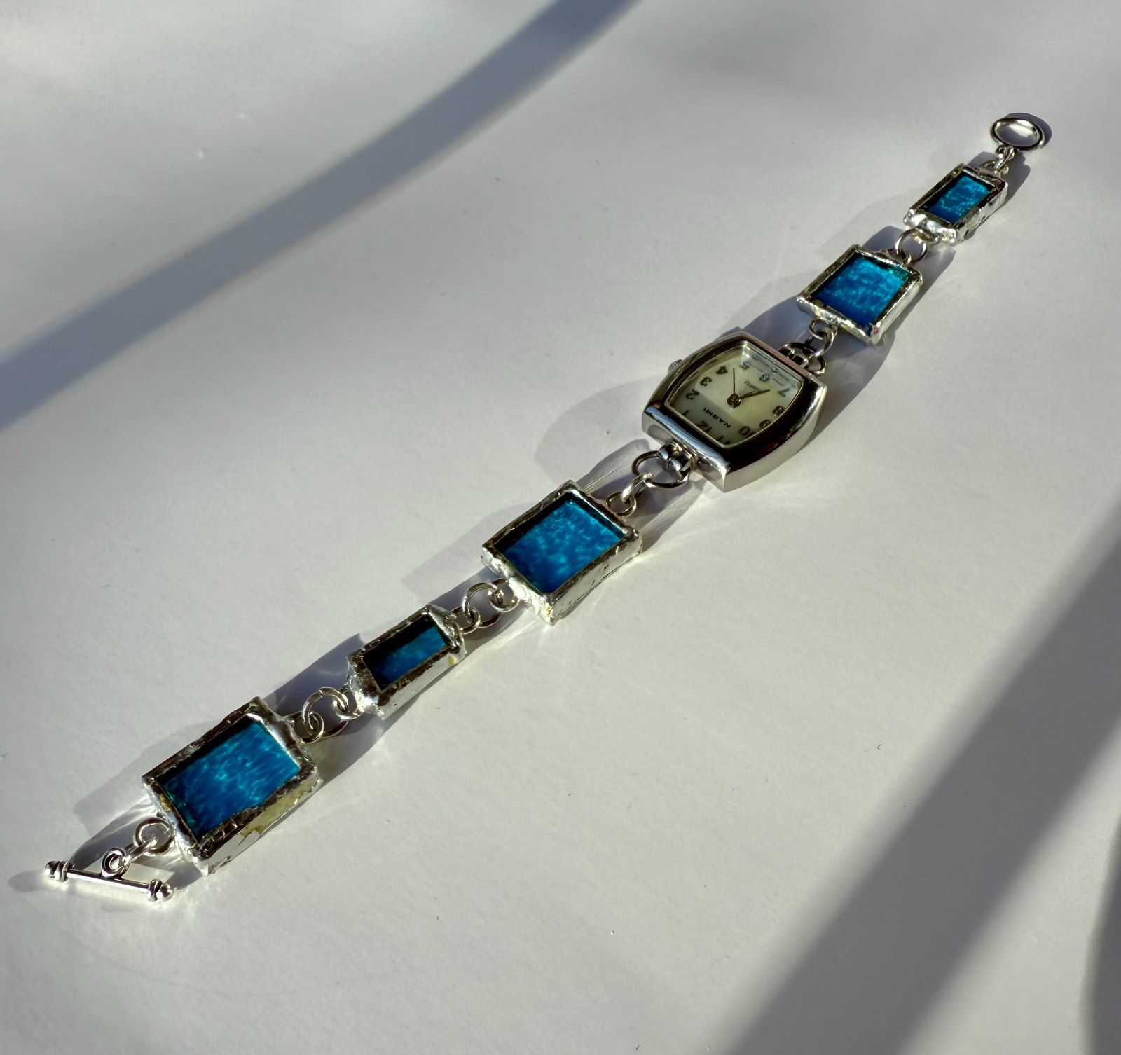 A handmade watch with a stained-glass beaded band in teal and aqua